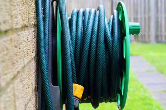 Garden hose coiled on a wall-mounted reel beside a house.